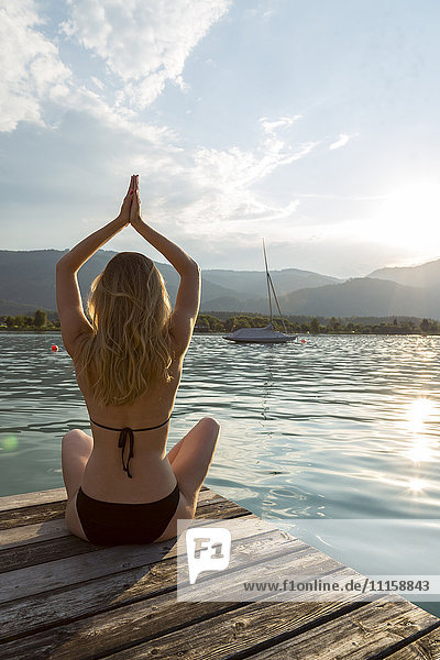 Austria  Sankt Wolfgang  woman in bikini in yoga pose sitting on jetty at lake