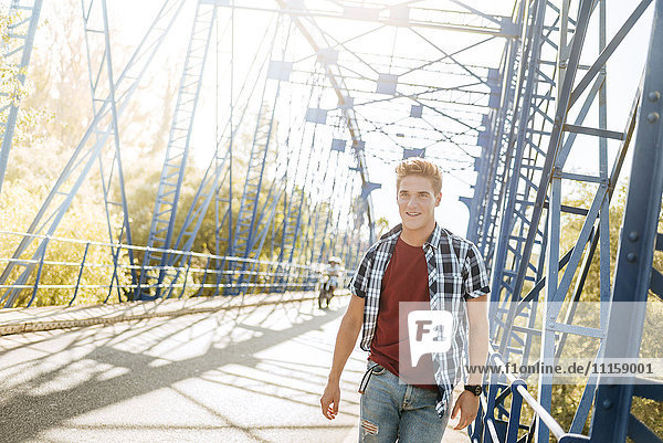 Lächelnder junger Mann  der auf einer Brücke geht.