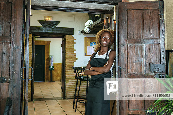 Lächelnde junge Kellnerin an der Tür einer Bar