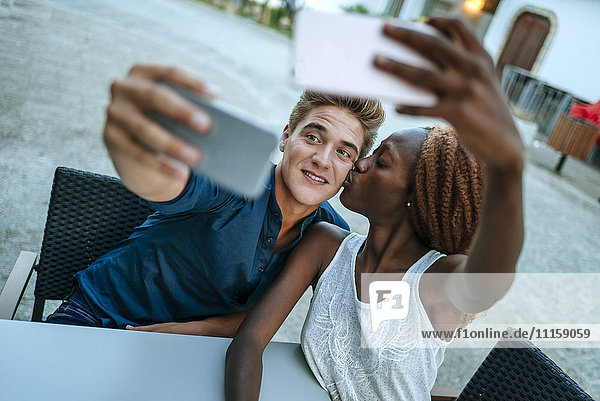 Young couple taking selfies at outdoor cafe