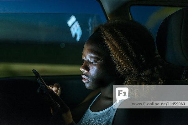 Junge Frau mit einem Smartphone im Auto bei Nacht