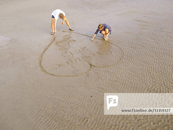 Paar am Strand zieht Herz in den nassen Sand
