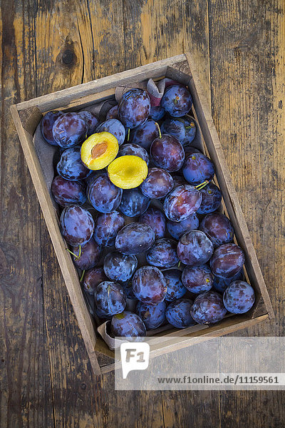 Wooden box of plums with a sliced one
