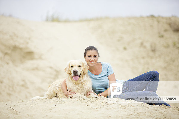 Smiling young woman with dog in sand