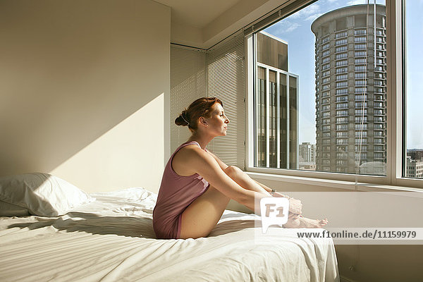 Woman sitting on bed looking out of window