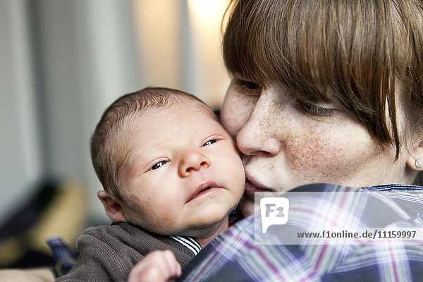 Freckled mother kissing her newborn baby son on the cheek