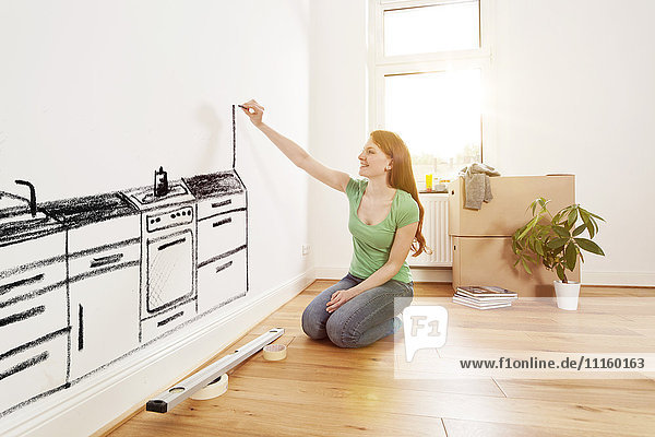 Young woman drawing a kitchen on a wall in new apartment