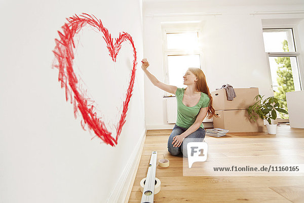 Young woman drawing a heart on a wall in new apartment