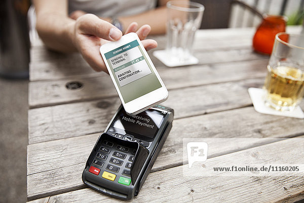 Hand mit Smartphone Handy bezahlen im Cafe