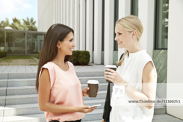 Two businesswomen talking outside during a coffee break