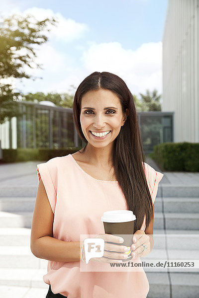 Porträt einer lächelnden Frau mit Kaffee zum Mitnehmen im Freien
