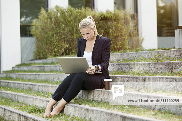 Young businesswomen sitting on stairs outside using a laptop