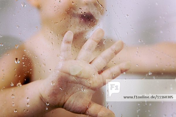 Hand des kleinen Jungen gegen nasse Glasscheibe in der Dusche