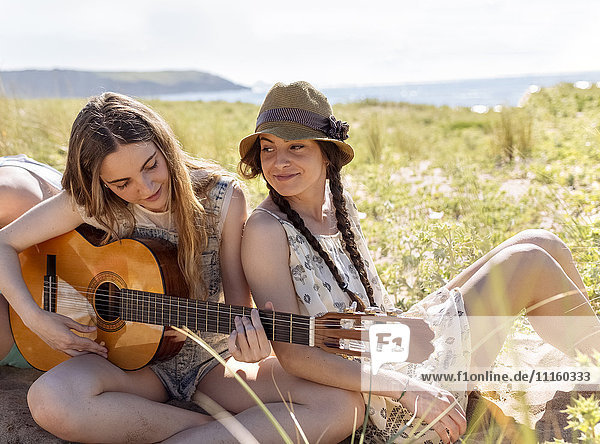 Teenagermädchen spielt Gitarre für ihre Freunde am Strand