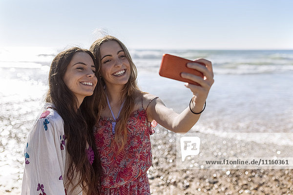 Two best friends taking selfie with smartphone on the beach