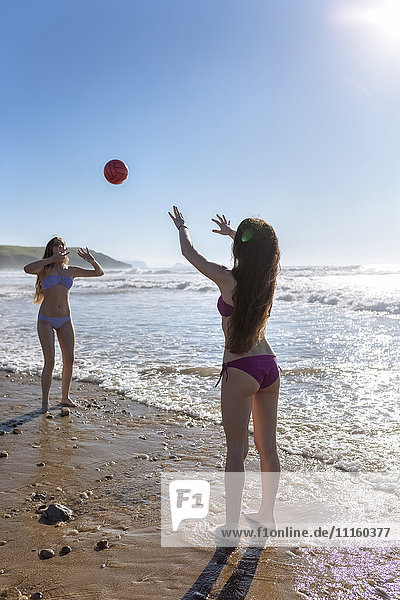Zwei Freunde spielen mit dem Ball am Strand.