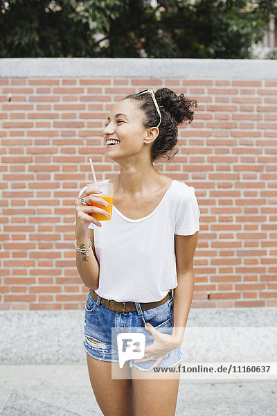 Happy young woman holding orange juice outdoors