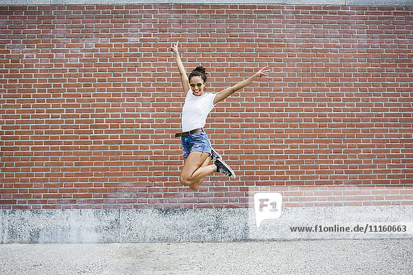 Exuberant young woman jumping in front of a brick wall