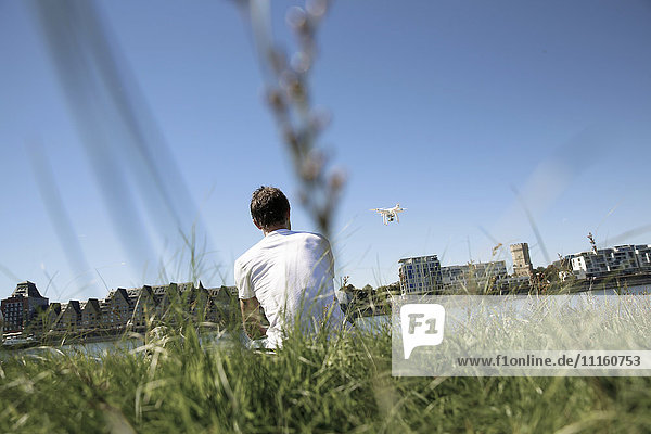 Ein reifer Mann  der im Gras sitzt und eine Drohne fliegt.