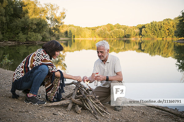 Senior couple lighting a campfire at a lake in the evening