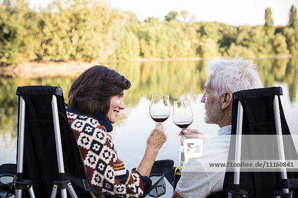 Seniorenpaar  das abends an einem See klirrende Weingläser trinkt