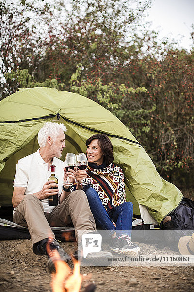 Seniorenpaar sitzt am Lagerfeuer mit Wein im Zelt