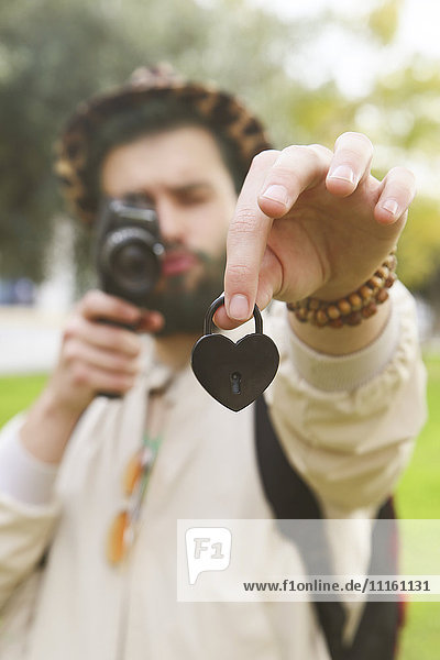 Man recording heart-shaped love lock in his hand with vintage video camera