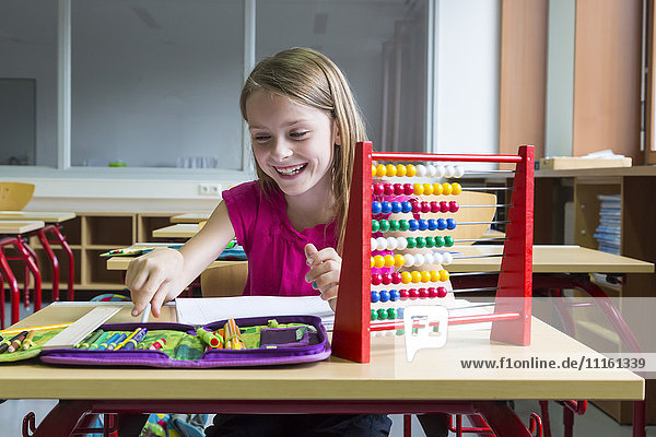 Smiling schoolgirl sitting at desk in her class