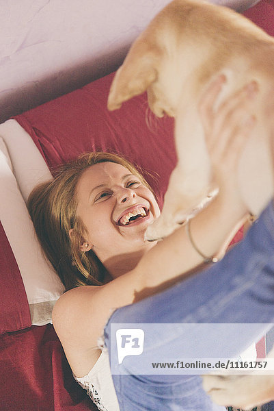 Glückliche junge Frau auf dem Bett liegend mit ihrem Labrador Retriever Welpen.