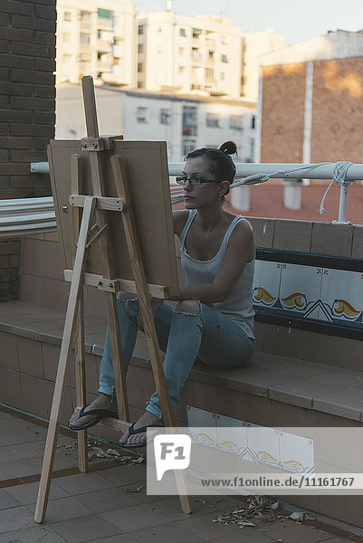 Junge Frau beim Zeichnen auf der Dachterrasse ihres Penthauses