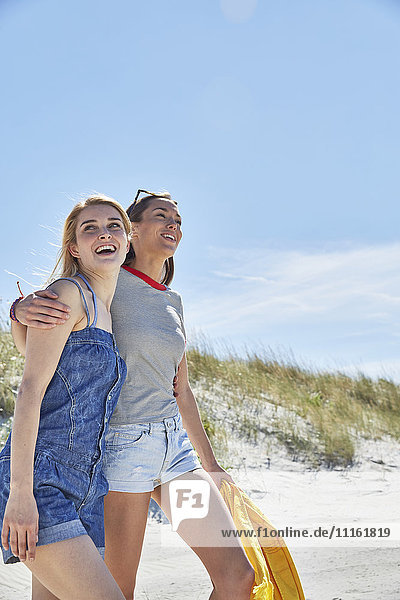 Zwei glückliche Freundinnen  die am Strand spazieren gehen.