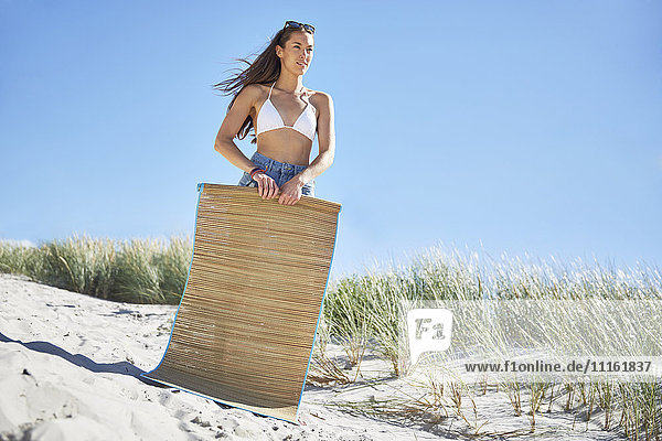 Junge Frau mit Strandmatte am Strand