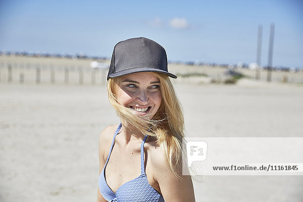 Fröhliche junge Frau mit Baseballmütze am Strand