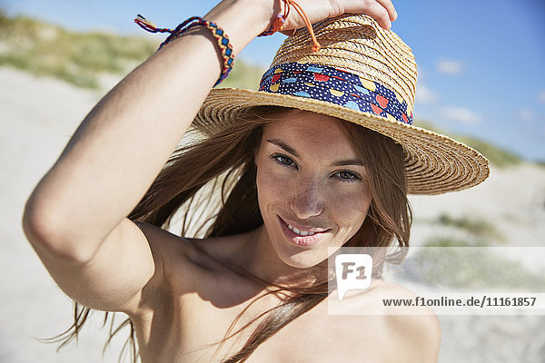 Porträt einer lächelnden jungen Frau mit Strohhut am Strand