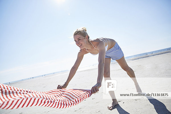 Junge Frau beim Ausbreiten des Handtuchs am Strand