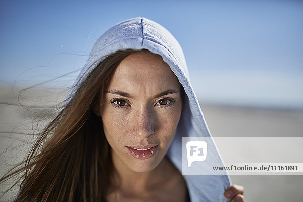 Lächelnde junge Frau mit Kapuze am Strand