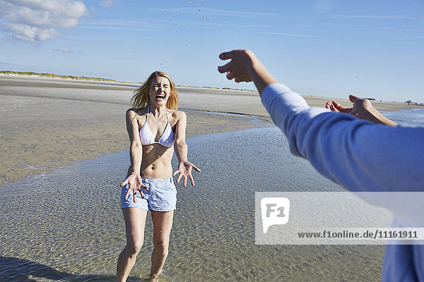 Glückliche junge Frau  die am Strand mit Wasser bespritzt wird.