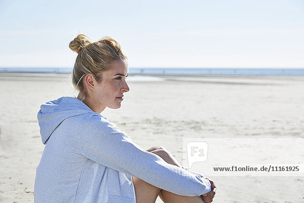 Junge Frau mit Kapuze am Strand sitzend
