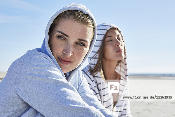 Zwei Freundinnen mit Kapuzenpullover am Strand