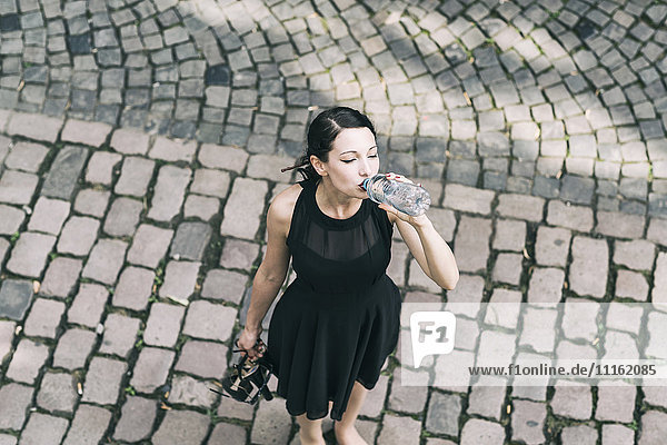 Young woman standing on cobblestones drinking water from bottle
