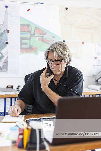 Mature man telephoning at desk in his office