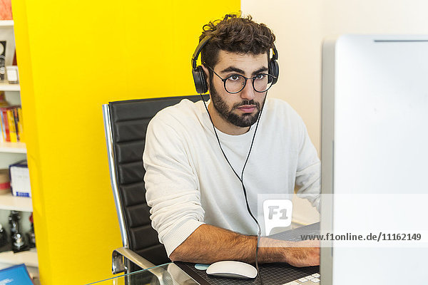 Junger Mann  der in einem Büro mit dem Computer arbeitet.