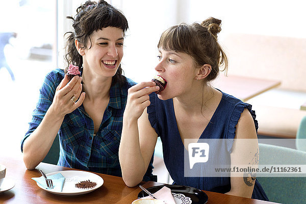 Zwei Freunde sitzen nebeneinander in einem Café und essen Tassenkuchen.