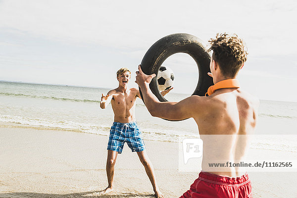 Zwei Freunde die mit Ball und Reifen am Strand spielen.