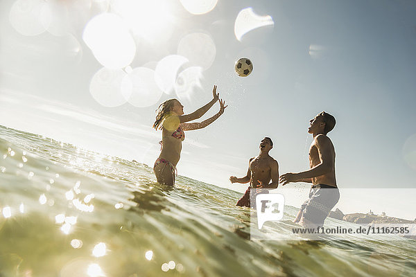 Freunde  die mit einem Ball im Meer spielen.