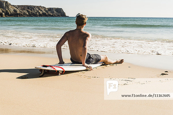 Teenage boy sitting on surfboard at the sea