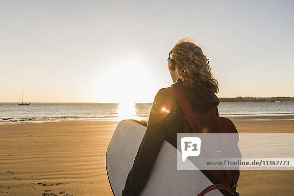 Teenage girl on the beach carrying surfboard