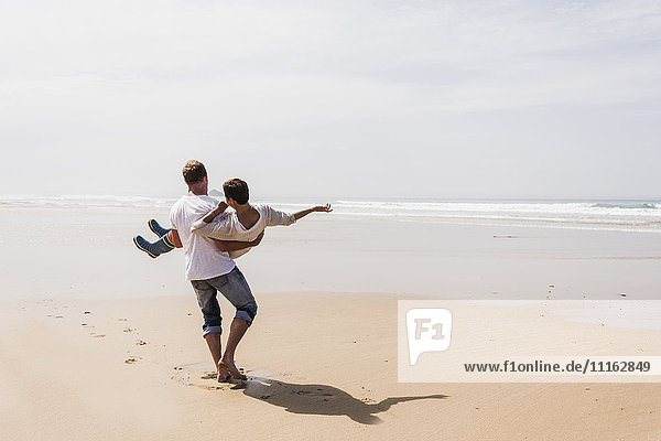 Mature man carrying his wife on the beach