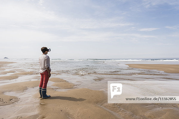 Mature woman standing on the beach wearing VR glasses
