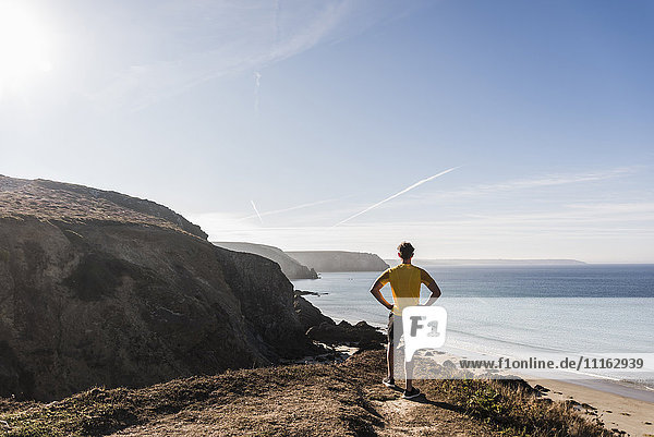 Frankreich  Halbinsel Crozon  sportlicher junger Mann an der Steilküste mit Blick auf die Landschaft